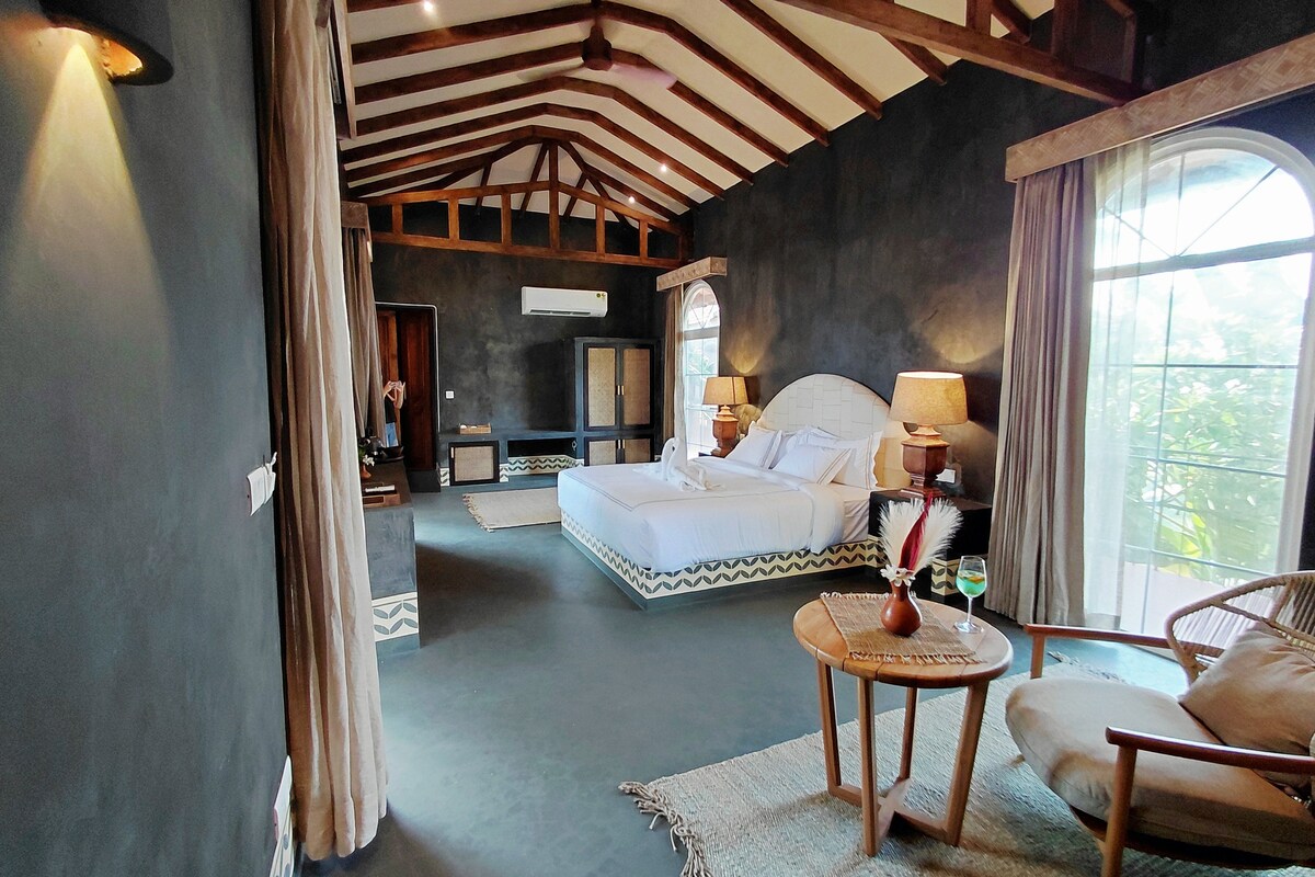 Un dormitorio con una cama grande, una zona de estar con una silla y vistas al exterior.