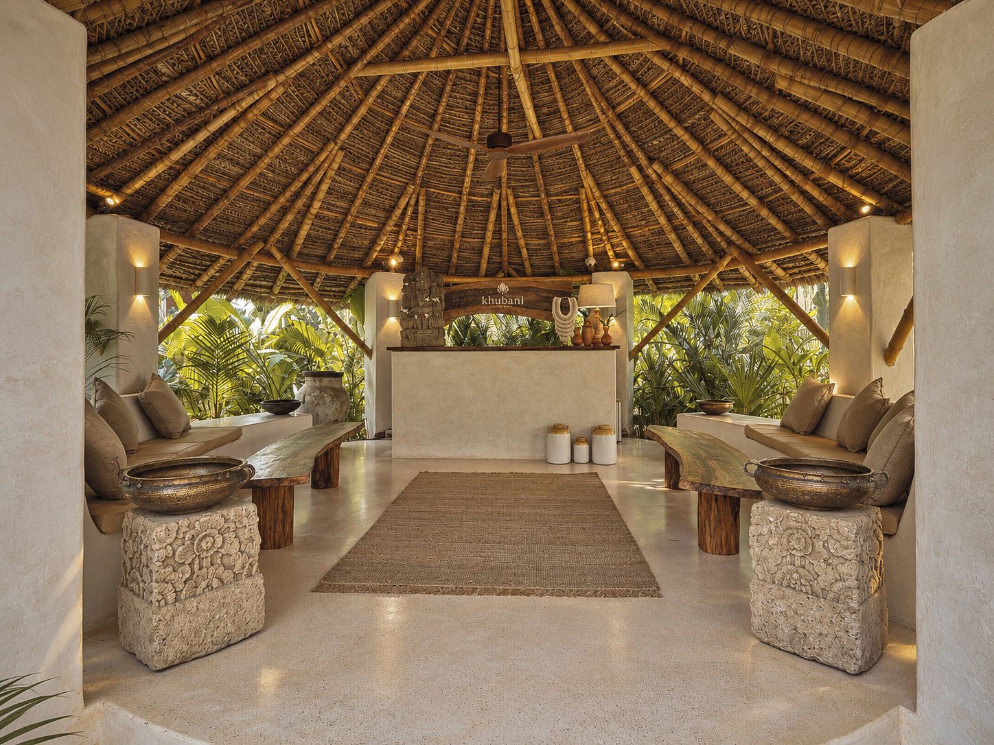 Un área de lounge con techo de paja, una recepción, asientos acolchados y elementos decorativos.