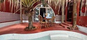 Un área de estar interior con una mesa, sillas, una pequeña palmera y una pared con estampado rojo y blanco.