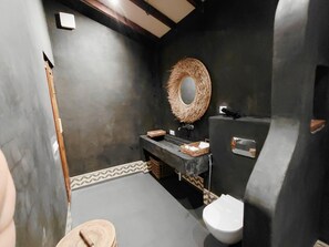 Un baño con una pared oscura, un espejo redondo, un lavamanos y un inodoro.