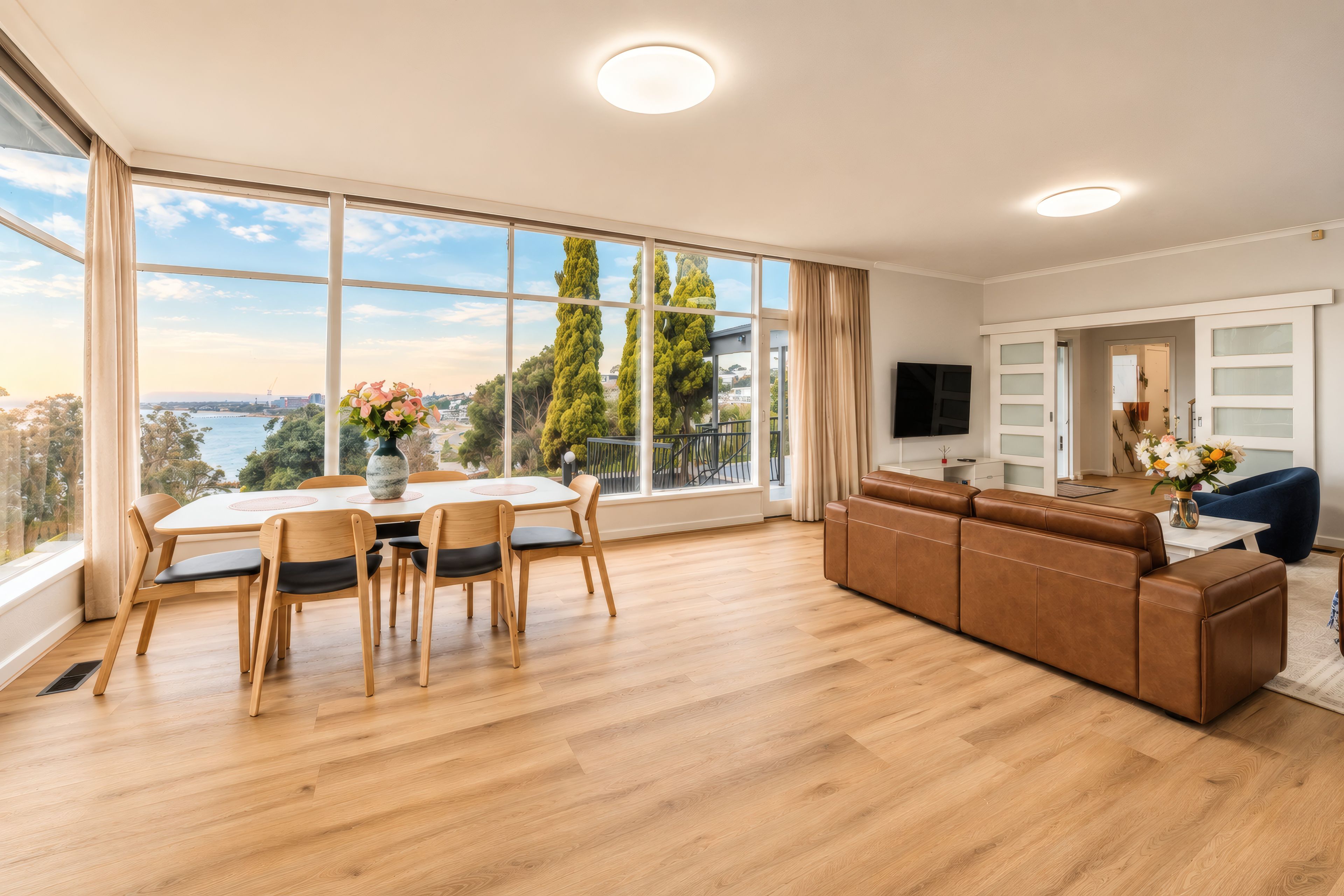 Ein großzügiges Wohnzimmer mit einem großen Esstisch, einer Couch und Blick auf das Meer.