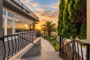 A modern building with a glass facade, a staircase with metal railings, and a view of the sunset.