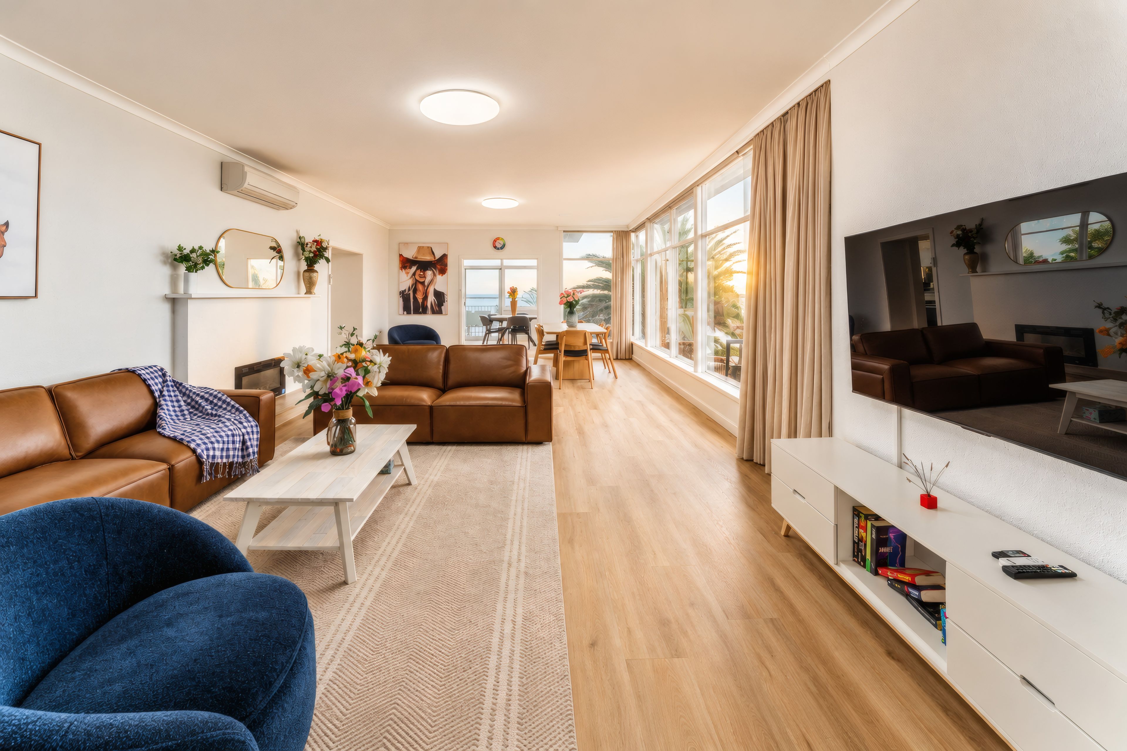 Una sala de estar moderna con un sofá, una mesa de centro y un televisor. Cuenta con un comedor con mesa y sillas. La habitación tiene ventanas amplias y vistas al exterior.