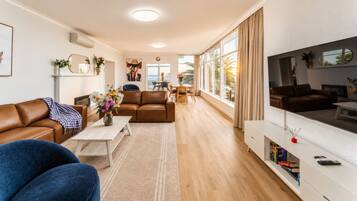 Una sala de estar moderna con un sofá, una mesa de centro y un televisor. Cuenta con un comedor con mesa y sillas. La habitación tiene ventanas amplias y vistas al exterior.