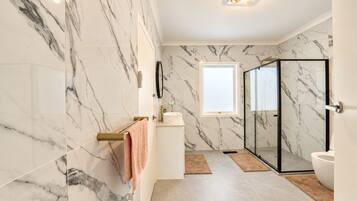 A bathroom with a marble wall, a glass shower enclosure, and a white sink.