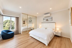 A bedroom with a large bed, bedside tables, a mirror, and a view of greenery outside.