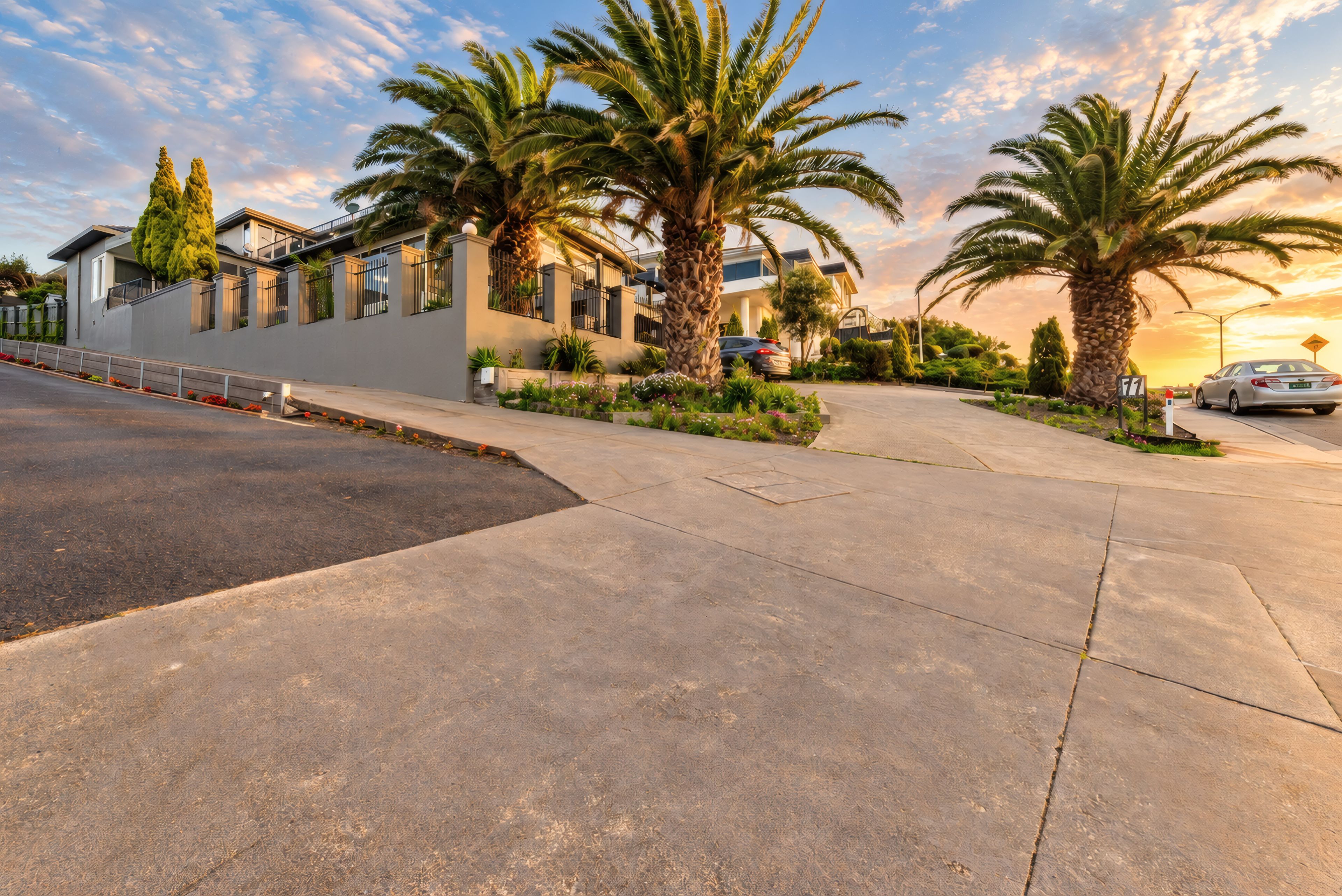A residential street with modern houses, palm trees, and a clear sky.
