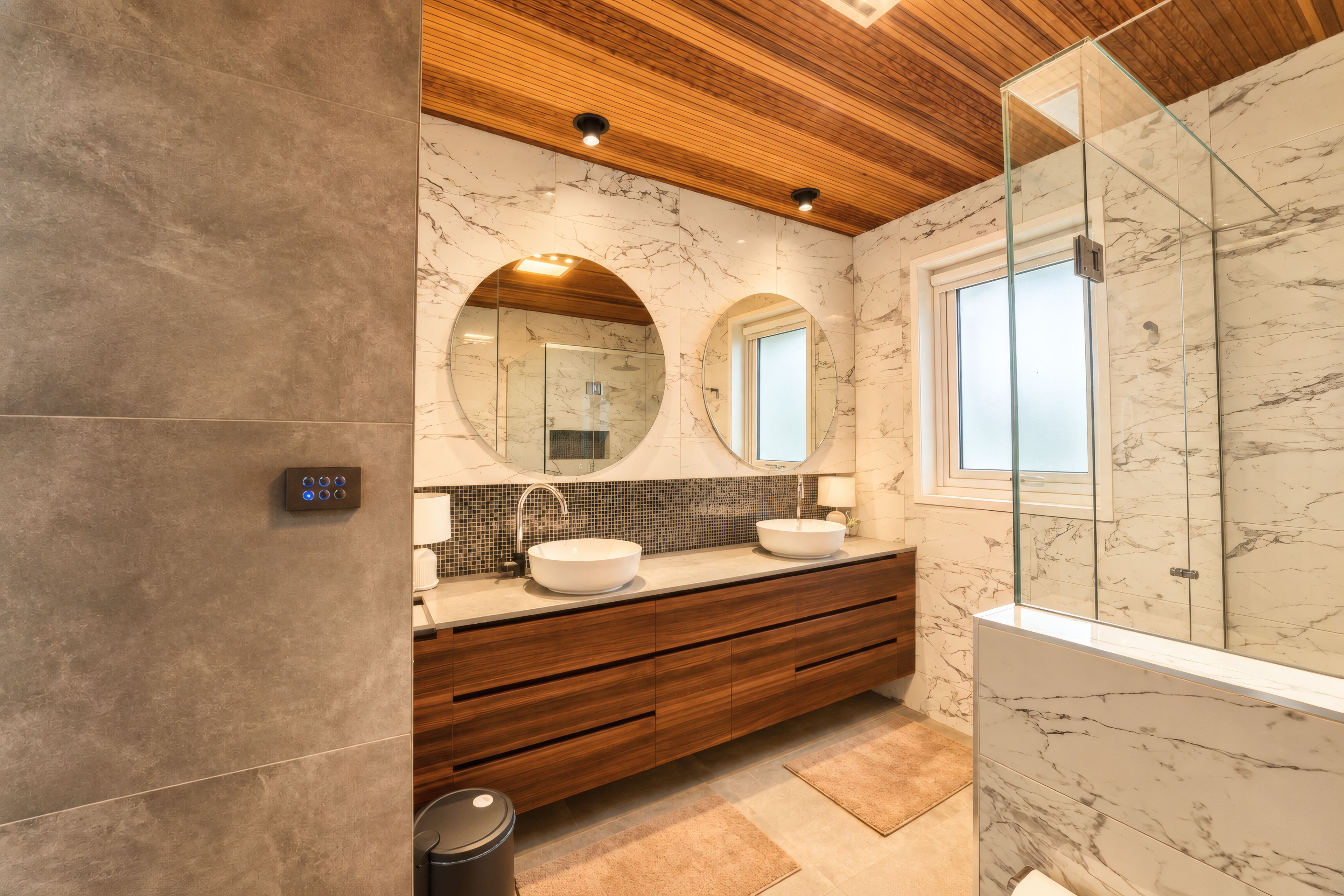 Een moderne badkamer met een houten plafond, marmeren wanden, een grote spiegel en een douche met glazen wanden.