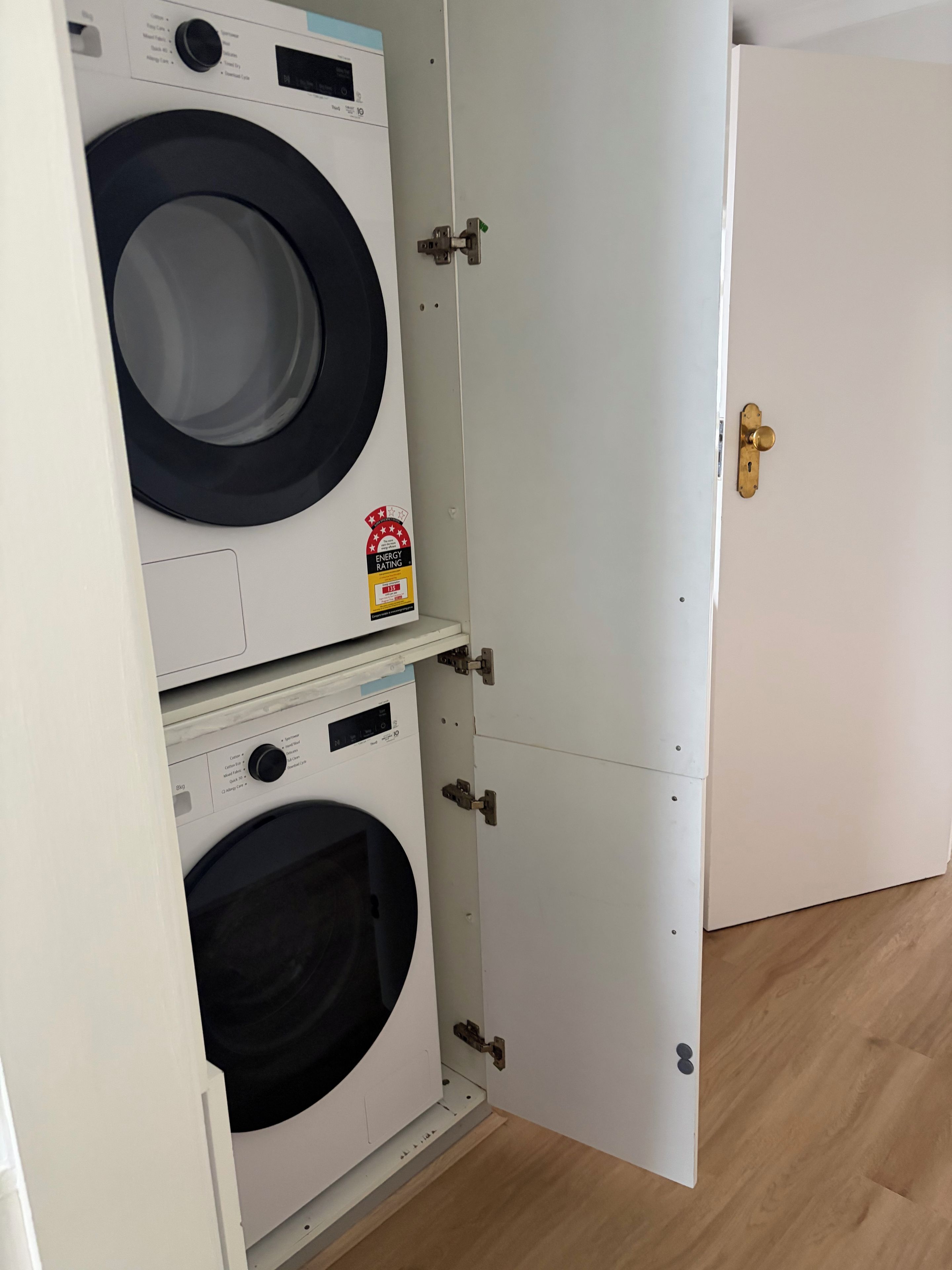 A compact, white laundry room with two front-loading washing machines and a door with a brass handle.