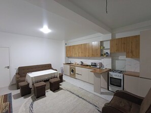 Een knus woongedeelte met een kitchenette, een eethoek met een tafel en stoelen, en een bank.