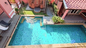 Une piscine rectangulaire dont les bords sont recouverts de carreaux, entourée d’une terrasse en bois et d’un petit jardin agrémenté de plantes et d’une structure en briques.