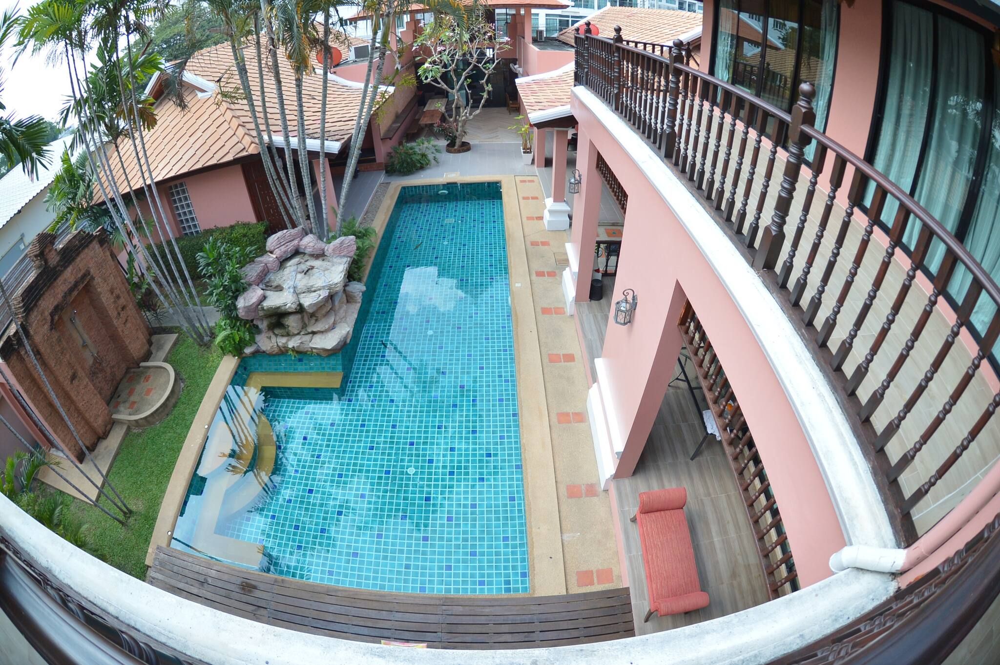 A rooftop pool with a tiled surface, surrounded by a wooden deck and a small rock feature.