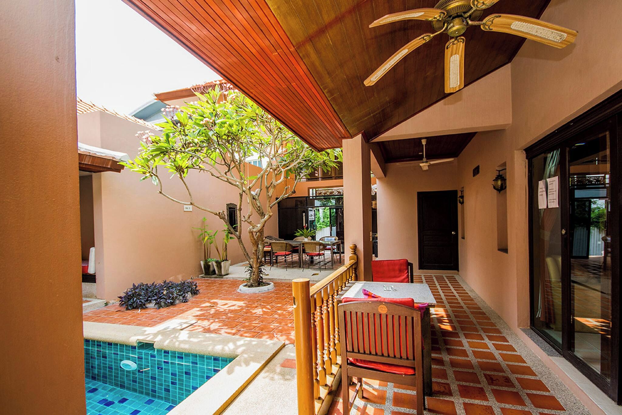 A covered outdoor area with a pool, wooden furniture, and a ceiling fan.