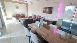 Une chambre d’hôtel moderne dotée d’une table à manger en bois, de sièges confortables, d’un téléviseur à écran plat et d’un réfrigérateur.