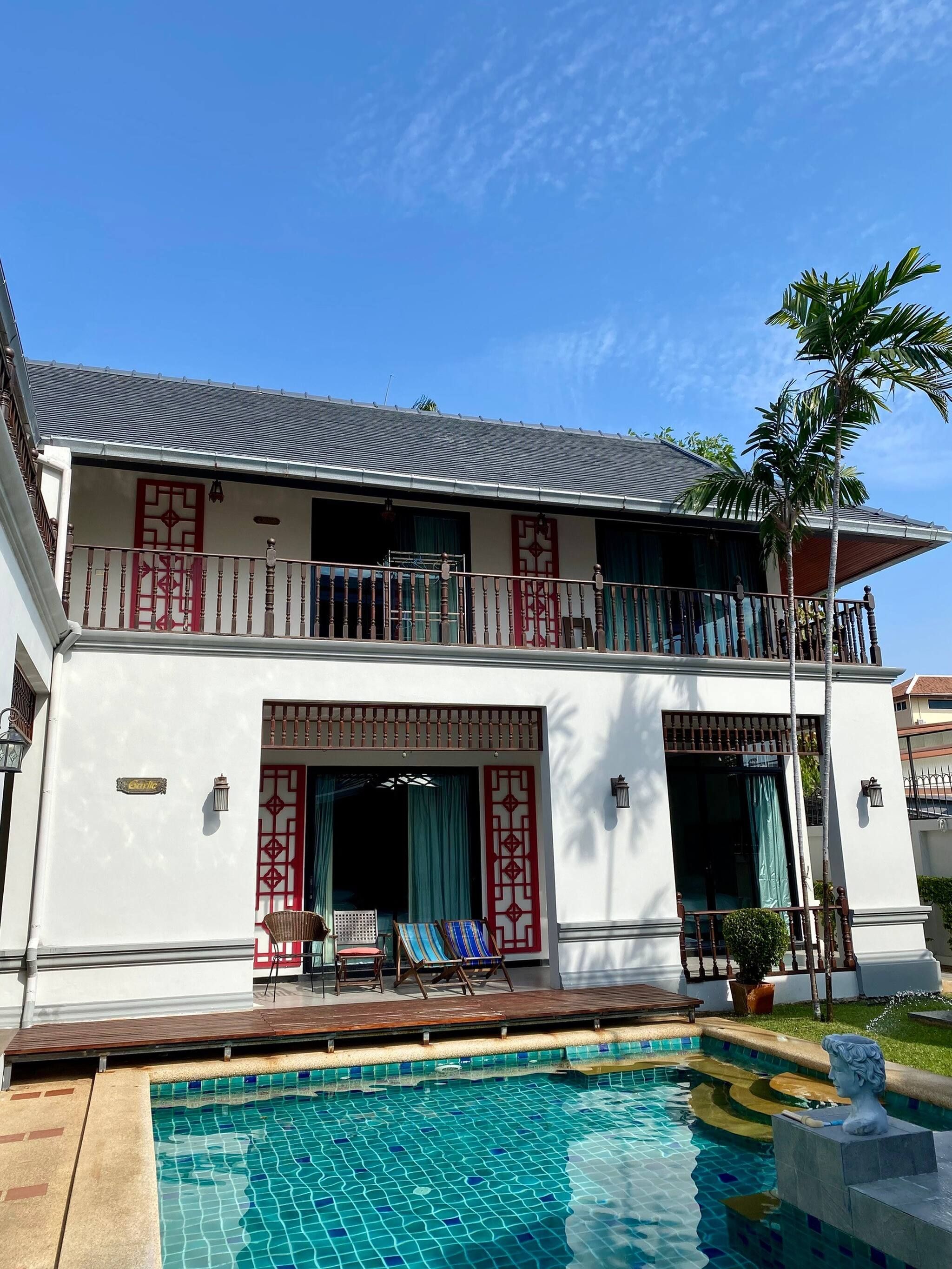 A two-story building with a swimming pool, balconies, and a palm tree.