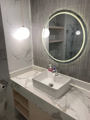 A bathroom with a marble vanity, a sink, a mirror with a circular frame, and a shower area. - Apartment in Pattaya (Pattaya City)