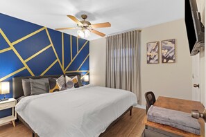 Une chambre d’hôtel équipée d’un lit, d’un bureau, d’un ventilateur de plafond et décorée avec des œuvres d’art.