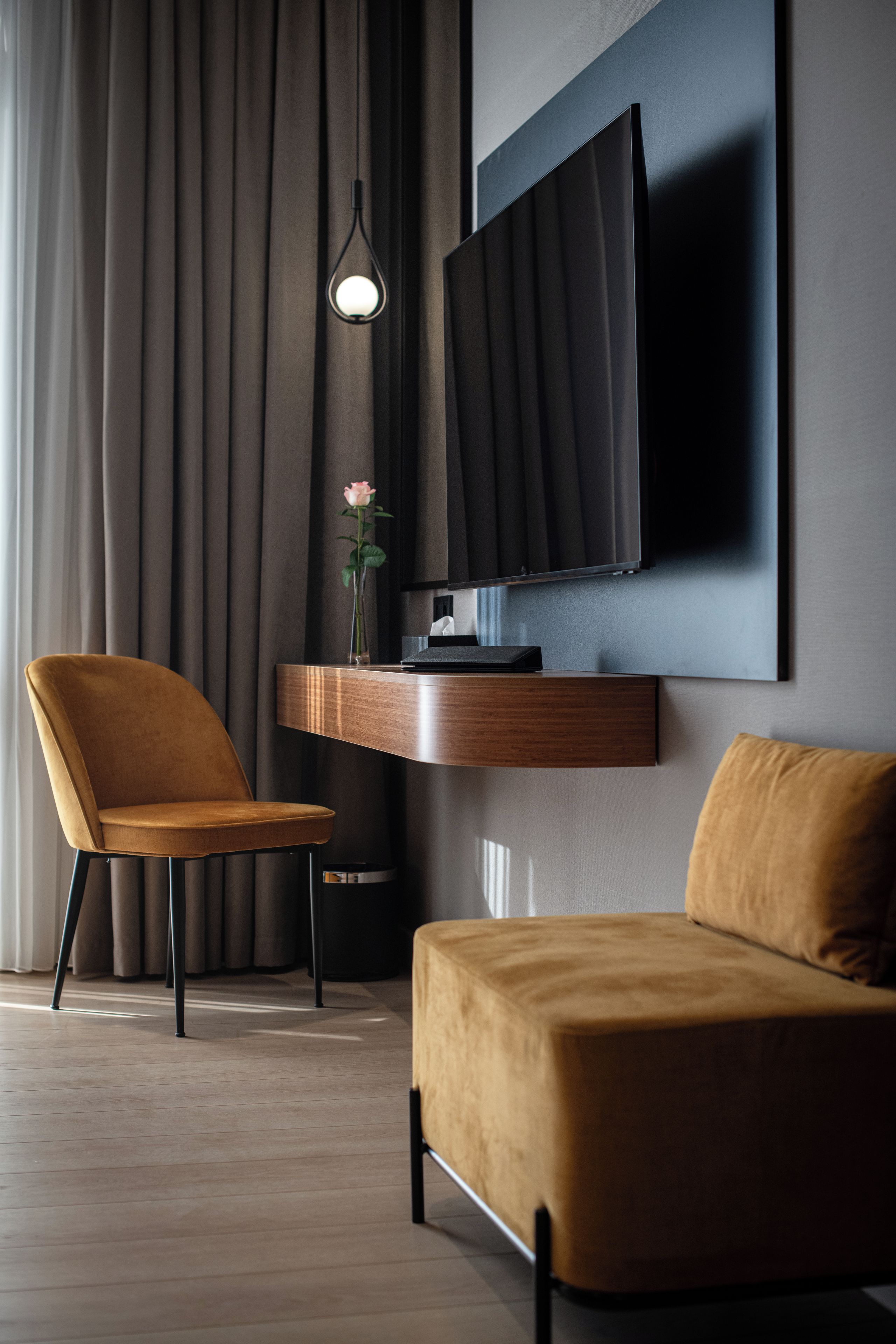 A modern living room with a sofa, a chair, a television mounted on a wall, and a small table with a vase.