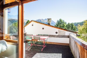 A balcony with a table and chairs, a wooden fence, and a view of mountains. - The Green Hut – Sunny Family Apartment Near St. Moritz & the Ski Slopes (Celerina/Schlarigna)