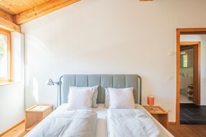 A bedroom with a wooden ceiling, a bed with two pillows, a bedside table, and a nightstand. - The Green Hut – Sunny Family Apartment Near St. Moritz & the Ski Slopes (Celerina/Schlarigna)