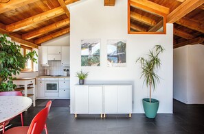 A modern kitchen with white cabinetry, a dining area with a red chair, and a potted plant. - La Cabane Verte – Sunny family apartment near St. Moritz & Ski Slopes (Celerina/Schlarigna)