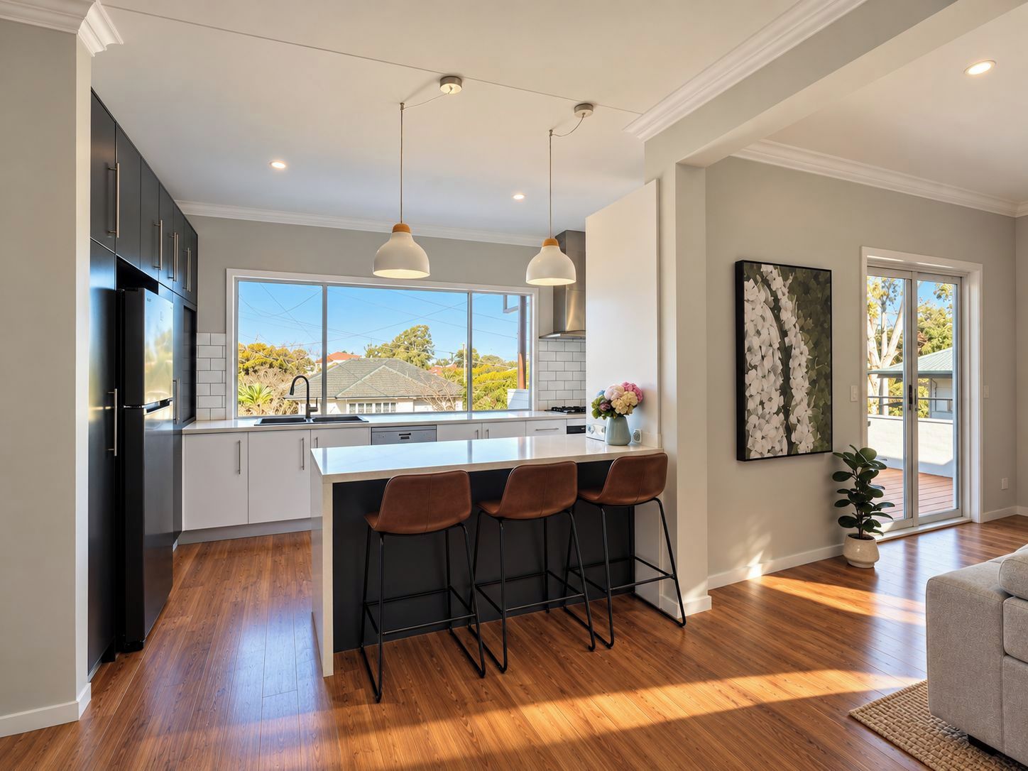 A modern kitchen with a large island, bar stools, pendant lighting, and a view of the outside.