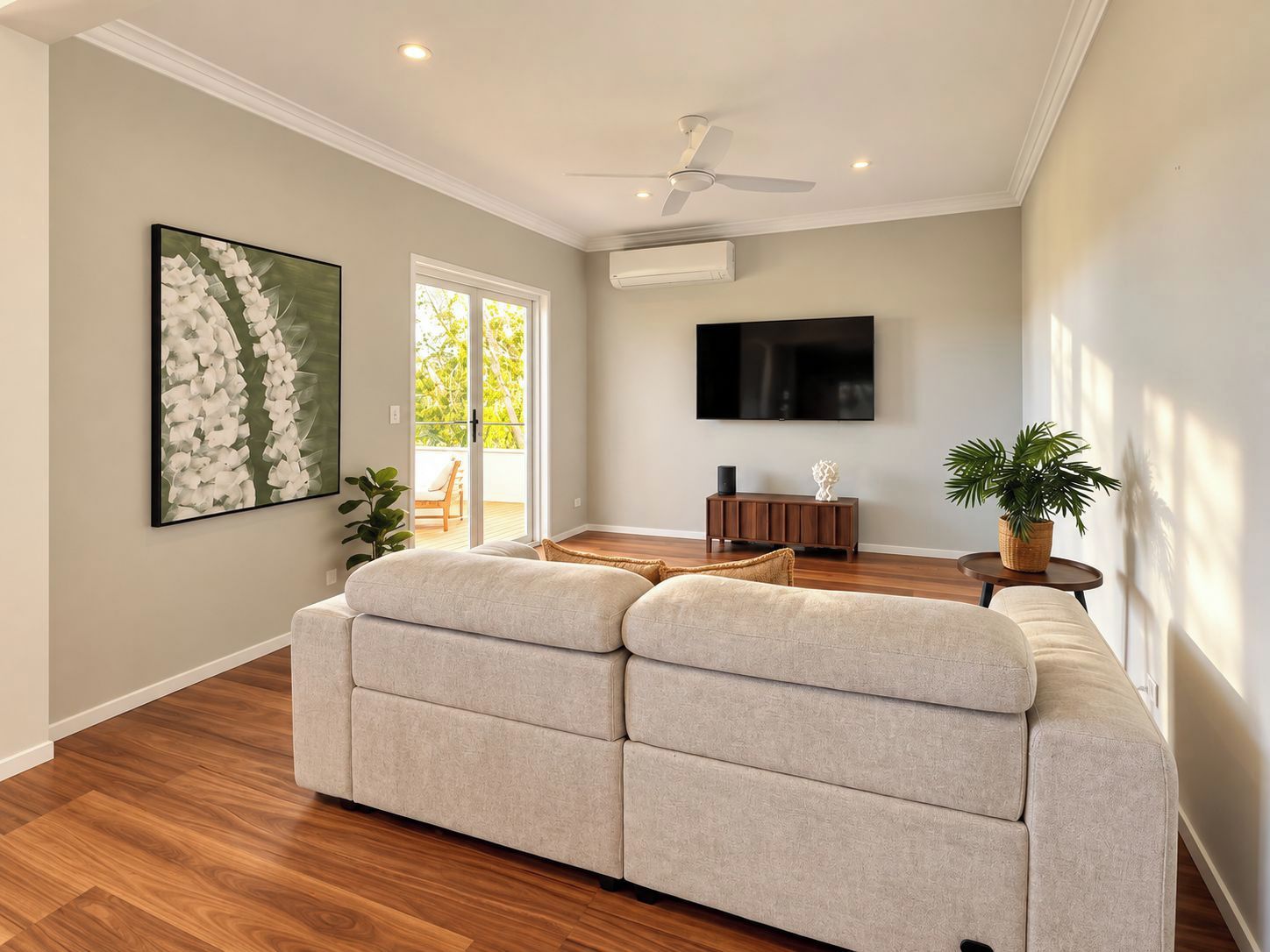 A living room with a beige sofa, a flat-screen TV, and a ceiling fan.