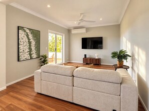 Ein Wohnzimmer mit einem beigen Sofa, einem Flachbildfernseher und einem Deckenventilator.