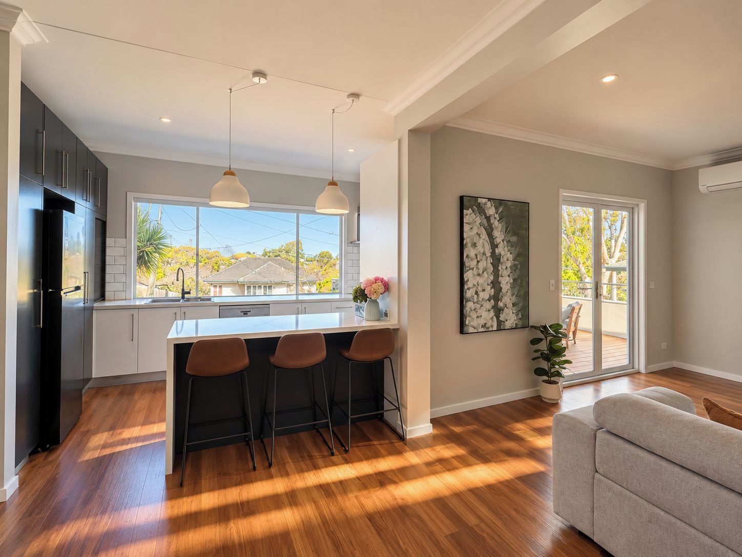 A modern kitchen with a central island, bar stools, pendant lighting, and a view of a residential area.