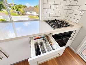 A kitchen with a gas stove, white cabinets, and a view of the neighborhood through a window. - The Ferricks |2BR Cosy Stafford Home (Stafford)