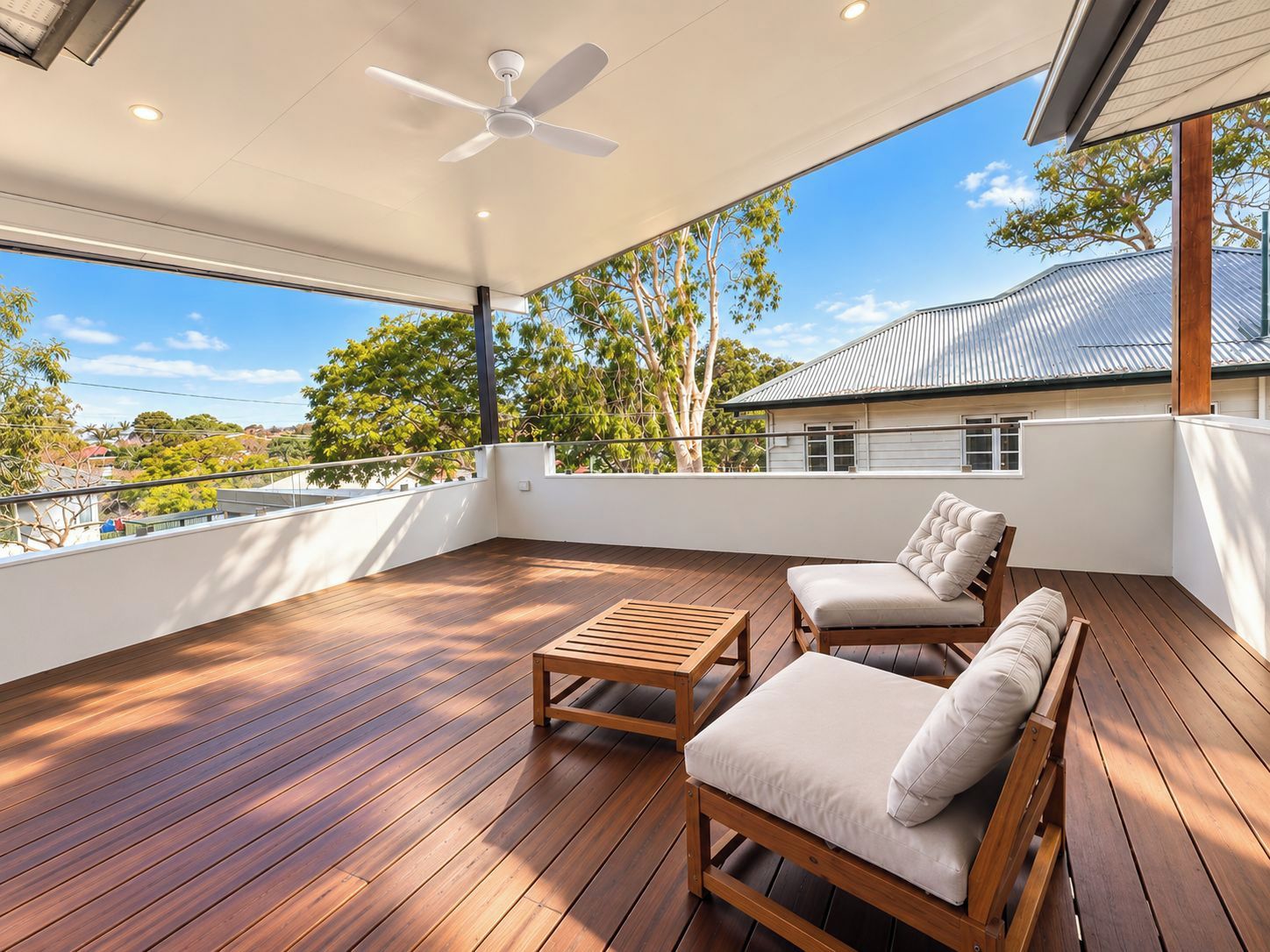 A spacious balcony with wooden flooring, a ceiling fan, and two cushioned chairs.