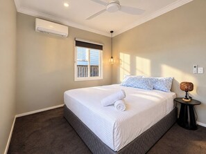A bedroom with a bed, a ceiling fan, an air conditioning unit, a window, and a bedside lamp. - The Ferricks |2BR Cosy Stafford Home (Stafford)