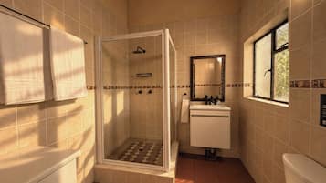 A bathroom with a shower, sink, toilet, and a window.
