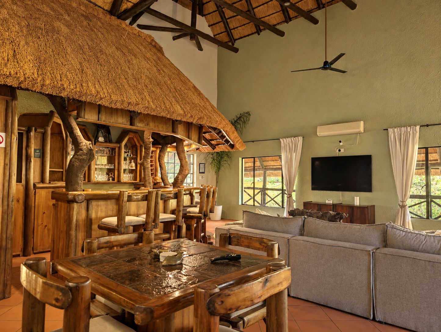 A rustic interior with a wooden dining table, chairs, a sofa, a TV, and a ceiling fan.