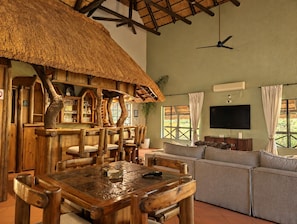 A rustic interior with a wooden dining table, chairs, a sofa, a TV, and a ceiling fan.