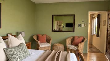 A bedroom with a bed, two wicker chairs, a mirror, and a television.