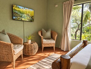Una habitación con una cama, dos sillones de mimbre, una mesita redonda con una planta y un cuadro en la pared.