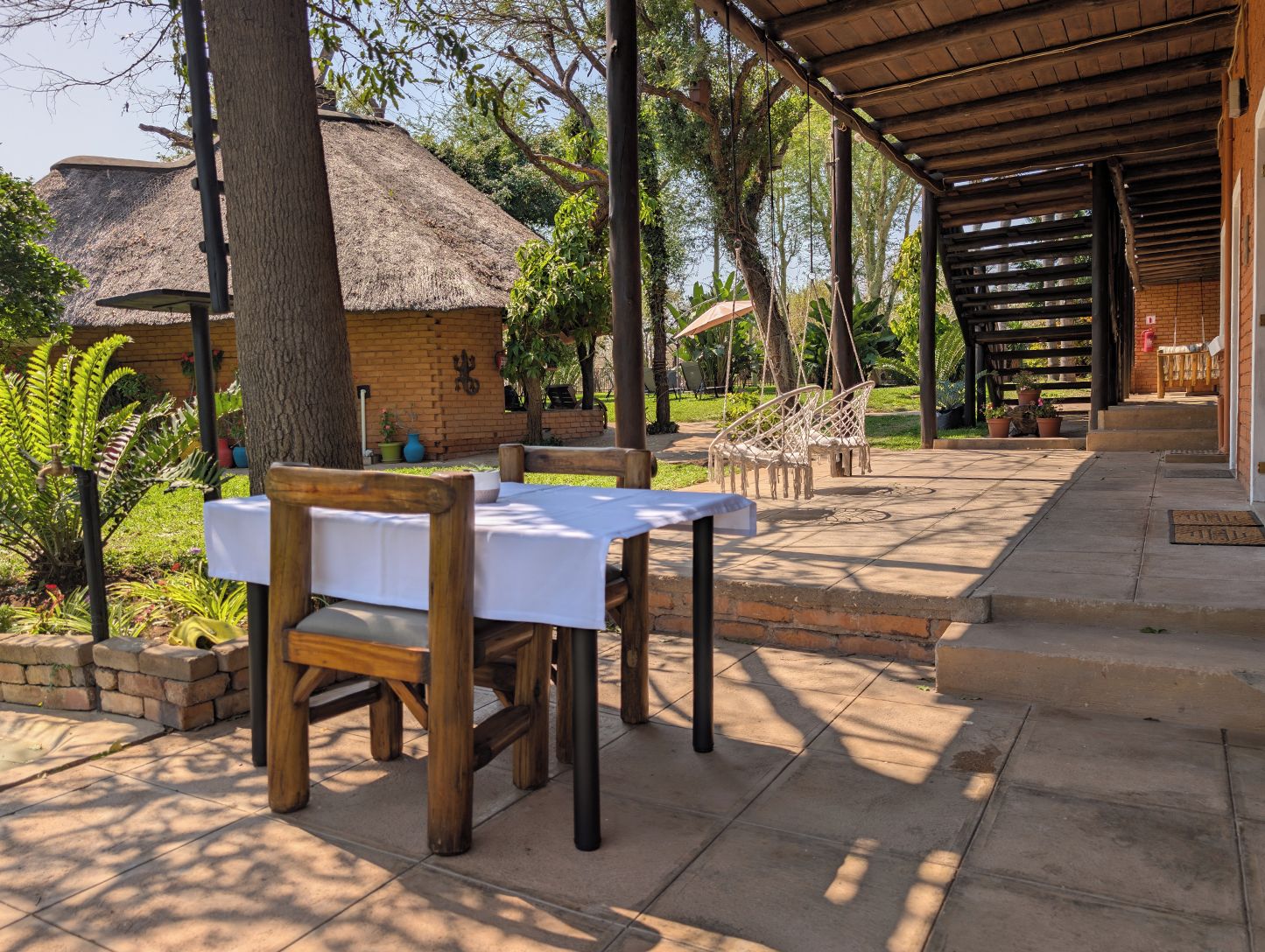 An outdoor dining area with wooden tables and chairs, a thatched-roof structure, and a covered seating area.