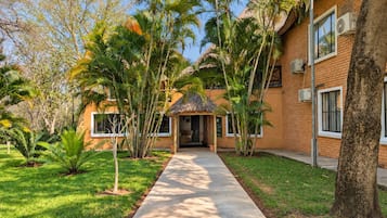Un edificio con fachada de ladrillo, un camino de hormigón y vegetación tropical.