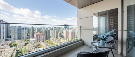 Un balcon avec vue sur la ville, une table en verre et des chaises en osier.