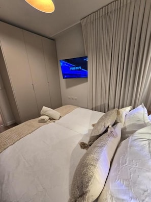A hotel room with a bed, a television mounted on the wall, and a curtain. - Biankini Royal suites (Jerusalem)