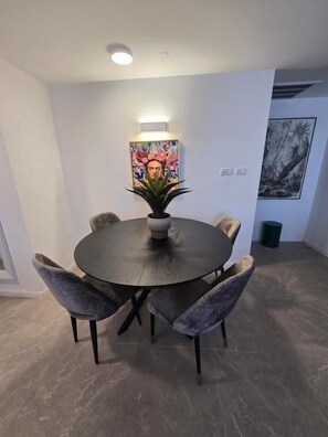 A dining area with a round table, four chairs, a potted plant, and two wall-mounted artworks. - Biankini Royal suites (Jerusalem)