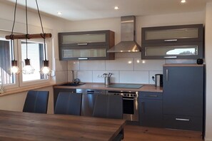A modern kitchen with built-in appliances, a dining area with a wooden table and chairs, and pendant lighting. - Holiday home with 1 bedroom (Elmstein \/ Iggelbach)
