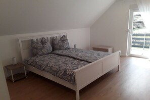 A bedroom with a sloped ceiling, a bed with patterned bedding, a bedside table, and a view through a door. - Holiday home with 1 bedroom (Elmstein \/ Iggelbach)