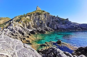 A rocky coastline with clear turquoise waters and a prominent stone structure on a hill. - VACATION HOME in CILENTO, ASCEA - ITALO & SILVIO (Campania)