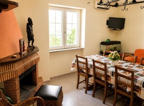 A dining area with a brick fireplace, a table with a floral tablecloth, and a television mounted on the wall. - VACATION HOME in CILENTO, ASCEA - ITALO & SILVIO (Campania)