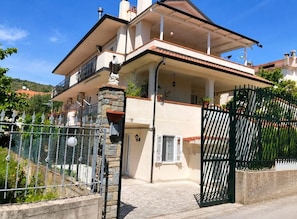 A two-story house with a balcony, a stone wall, and a gated entrance. - VACATION HOME in CILENTO, ASCEA - ITALO & SILVIO (Campania)