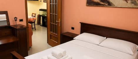 A hotel room with a bed, a desk, a chair, a television, and a painting on the wall.