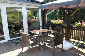 An outdoor patio with a glass table and wicker chairs, a wooden deck, and potted plants. - Holiday home with 2 bedrooms (Winterberg-Niedersfeld)