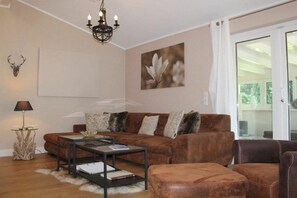 A living room with a brown sofa, a coffee table, a chandelier, and a painting on the wall. - Holiday home with 2 bedrooms (Winterberg-Niedersfeld)
